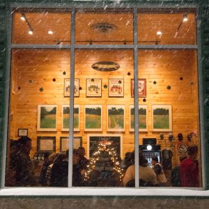 An outside looking in shot of the taproom lit up from the holiday sweater party going on inside"