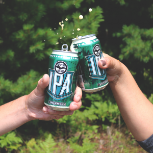 Two hands toasting with green cans of beer labeled IPA"